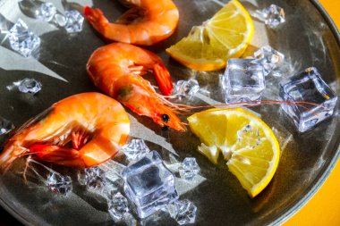 Gri tabakta limonlu ve buzlu kırmızı karides ve sarı arka plan. Moda renkleri. İzometrik biçimdeki minimalist kavram