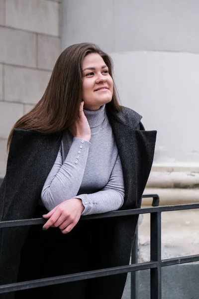 Retrato de una joven morena caucásica sonriente. Empresaria al aire libre en el centro de negocios. Ciudad urbana estilo de vida urbano. Abrigo largo y cabello. —  Fotos de Stock