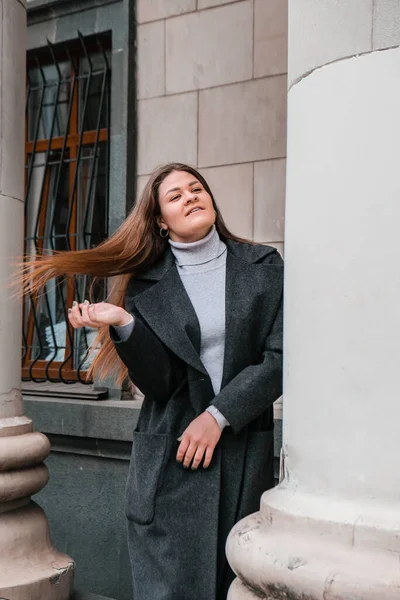 Retrato de jovem mulher morena branca sorridente. Mulher de negócios ao ar livre no centro de negócios. Estilo de vida urbano da cidade. Casaco comprido e cabelo. — Fotografia de Stock