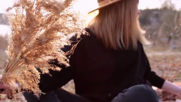 Femme blonde caucasienne agitant pampas herbe avec chapeau beige en pull noir dans la campagne. Heure d'or, Cotagecore. Voyage local. Une vie lente. Santé mentale — Video