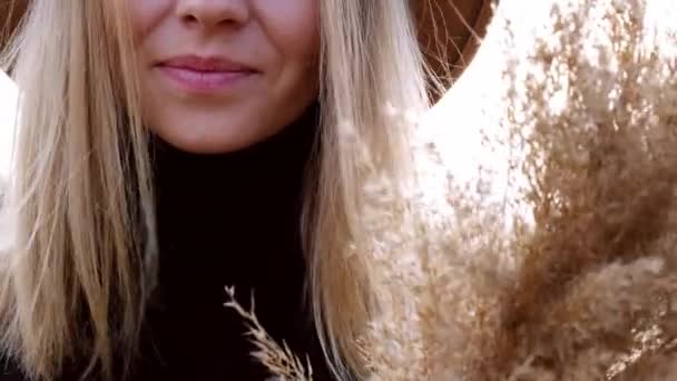Mulher loira europeia sorrindo com chapéu bege em camisola preta no campo. Hora de ouro, cottagecore. Viagens locais. Uma vida lenta. Saúde mental. Grama Pampas — Vídeo de Stock