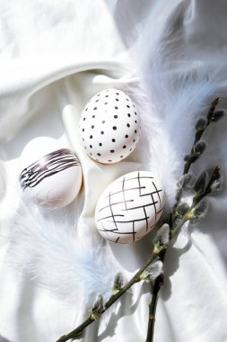 Trendy colored stylish Natural easter eggs, feathers, pussy willow branches on rustic cloth on white silk fabric. Flat lay. Easter still life. Table plate