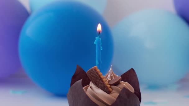 Dulce sabroso cupcake de chocolate con vela ardiendo sobre fondo festivo azul. Llama, soplando concepto de fiesta de cumpleaños feliz. Delicioso pastel de cumpleaños — Vídeos de Stock