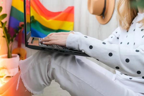 Jonge millennial hippie vrouw zit op het balkon met behulp van laptop. LGBTQ regenboogvlag op achtergrond. Online onderwijs onderwijs. Werk vanuit huis. Modern kantoor. — Stockfoto