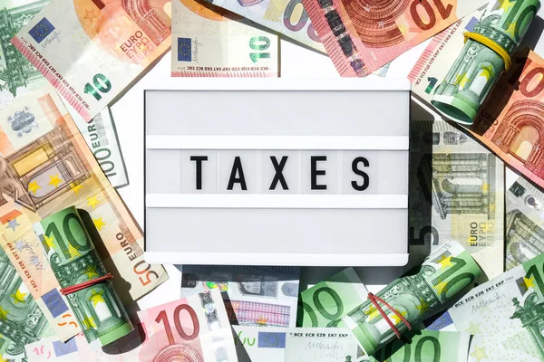 在欧元钞票周围用黑色字母写着 Taxes 字样的光盒板 纳税和申报概念 储蓄和腐败 现金结单 — 图库照片