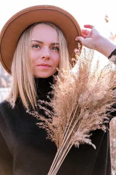 Європейська блондинка з бежевим капелюхом у чорному светрі в сільській місцевості. Золота година, коттагекор. Місцеві подорожі. Повільне життя. Розумове здоров'я. Трава пампасу — стокове фото