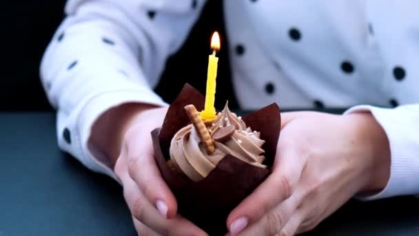 Mani femminili che fanno deliziosi cupcake al cioccolato con crema su sfondo scuro. Muffin al cioccolato fatto in casa. Torta di compleanno con candela accesa. Fiamma. Soffiando. — Video Stock