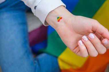 Bileğine gökkuşağı şeklinde kalp şeklinde bir bayrak çizen bin yıllık genç beyaz hippi kadının yakın çekimi. Gökkuşağı renk dövmesi, LGBTQ gurur ayının sembolü. Eşit haklar