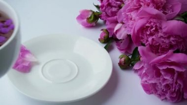 Pembe şakayık çiçekli 4K yaratıcı düzen. Parlak masada bir fincan çay tutan kadın. Bahar mevsimi sevgililer günü, kadın, anne, 8 Mart bayramı, romantik kahvaltı. Tarz sahibi blog yazarı.