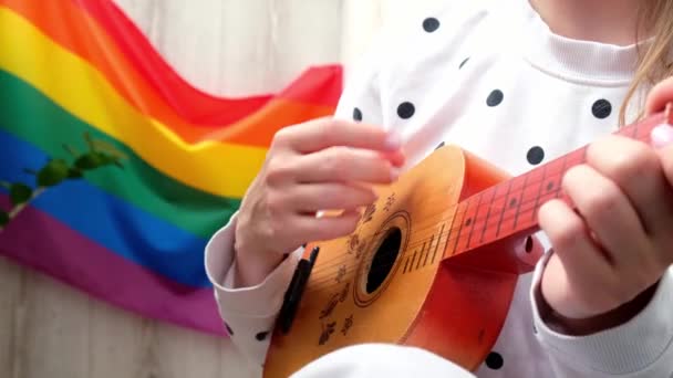 4k Jovem mulher hippie milenar sentado na varanda tocar guitarra. Lição de música e cantor sentado. Bandeira do arco-íris LGBTQ no fundo. Aulas de música online. Tocar instrumento e desfrutar de músicas e — Vídeo de Stock