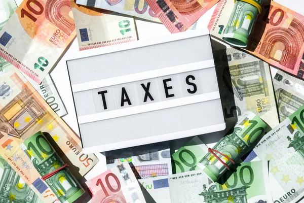 Lightbox board with word TAXES in black letters around Euro banknotes. Tax payment and filing concept. Money, Business, finance, investment, saving and corruption. Cash bill