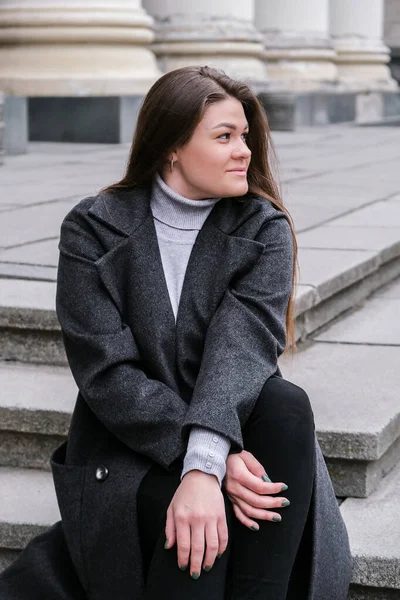 Retrato de una joven morena caucásica sonriente. Empresaria al aire libre en el centro de negocios. Ciudad urbana estilo de vida urbano. Abrigo largo y cabello. —  Fotos de Stock