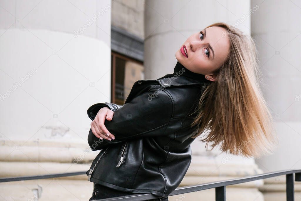 Portrait of young blonde woman with red lips wearing leather jacket on corporate building stairs. Career businesswoman. Urban street city lifestyle