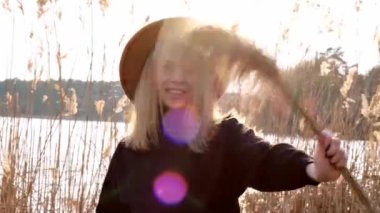 Milenyum kadını 4k Kafkasyalı sarışın kadın kırsalda siyah kazaklı bej şapkalı otlar sallıyor. Altın saat, Cottagecore. Yerel seyahat. Yavaş yaşam. Ruh Sağlığı