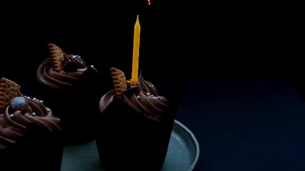 Mãos femininas fazendo deliciosos cupcakes de chocolate com creme no fundo escuro. Bolinho de chocolate caseiro. Bolo de aniversário com vela queimando. Chama. Sopro.. — Vídeo de Stock