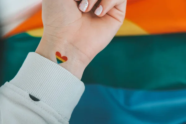 Zbliżenie młodej białej hipisowskiej hipiski z tęczową flagą w kształcie serca namalowaną na nadgarstku. Tęczowy tatuaż, symbol dumnego miesiąca LGBTQ. Równe prawa — Zdjęcie stockowe