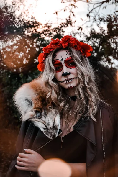 Buon Halloween. Spaventato orribile femmina seduta in abito speciale, indossa teschio di argilla bianca, trucco professionale teschio di zucchero per sembrare spettrale, indossa vestiti neri giocando con pelliccia di volpe — Foto Stock