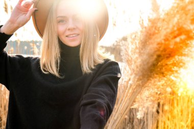 Kırsalda bej şapkalı, siyah kazaklı Avrupalı sarışın kadın. Altın saat, Cottagecore. Yerel seyahat. Yavaş yaşam. Akıl sağlığı. Pampas otu