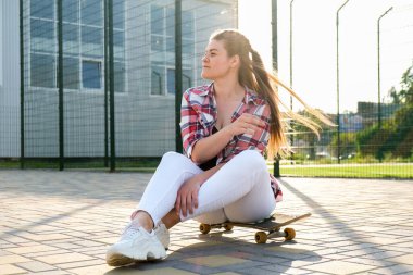 Genç milenyum kadın hippi kaykayda oturuyor. Yaz pateni seansları. Parkta sörf tahtasıyla gezen bir kadın. Kaygısız kadın patenci. 20 'li yaşlarda. Özgürlüğün tadını çıkarıyor.
