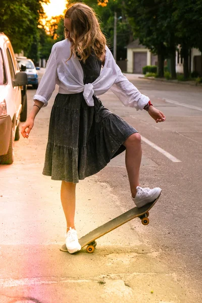 Millennial žena v šatech na skateboardu na ulici. Bruslařka na dlouhém prkně. Super skateboardistka při západu slunce. Carefree fena bruslařka 20s těší svobodu mládež životní styl Hobby — Stock fotografie