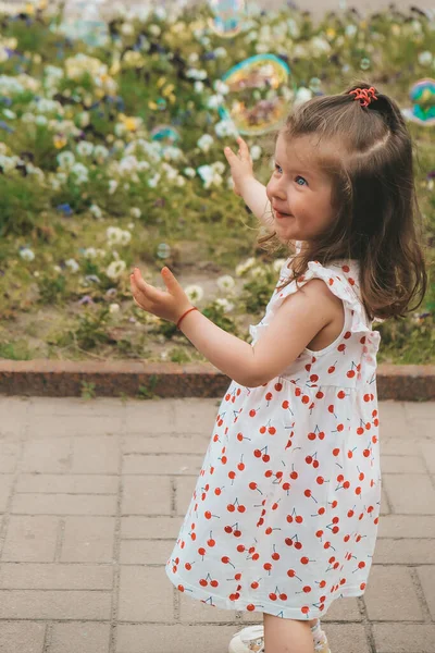 Een vrolijk meisje vangt zeepbellen met haar handen en lacht. Gelukkige jeugd, zomertijd. Portret van een jong peutermeisje — Stockfoto