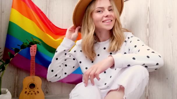 4k Ung blond tusenårig hippie kvinna skickar blåser kyss med regnbåge hbtq flagga hemma balkong. Fred och frihet symbolen för hbt, spendera och dela kärleksfull tid. Stödja hbtq-grupper. — Stockvideo