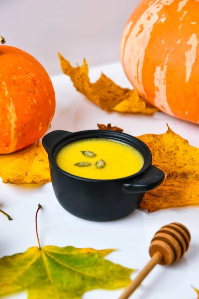 Autumn food. Pumpkin puree soup, leaves. Autumn harvest, pumpkins, leaves on grey as abstract background. Thanksgiving day. Seasonal food. Vegetarian