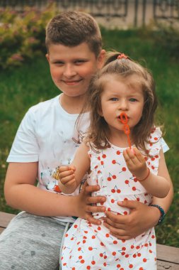 Neşeli bir kız sabun köpüğünü elleriyle yakalar ve kardeşiyle güler. Mutlu çocukluk, yaz zamanı. Küçük bir kızın portresi.