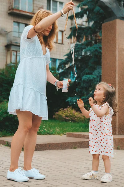 Jonge moeder die buiten met haar dochter speelt. Gelukkige jeugd, zomertijd. Portret van een jong peutermeisje — Stockfoto