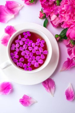 Pembe şakayık çiçekleri ve parlak masa üzerinde bir fincan çayla yaratıcı bir düzen. Bahar mevsimi sevgililer günü, kadın, anne, 8 Mart bayramı, romantik kahvaltı. Şık bir blog yazarı. Tebrik kartı. Davetiye. Günlük postası