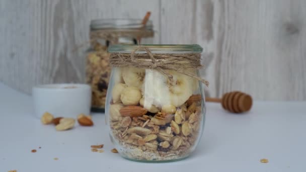 4k Healthy breakfast. Oatmeal Granola with greek yogurt pouring and nuts banana muesli in jars on light background. Vegan, vegetarian and weight loss diet concept. Detox menu. — Stock Video