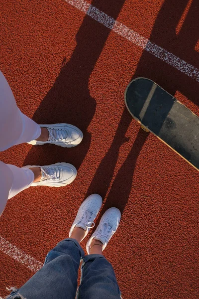 友人を閉じます女の子のスケートボードの足は日没でスケートボード。サンバックライトと自由の反逆者の独立した概念。アクティブなボード趣味のための支出日. — ストック写真