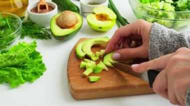 Taze yeşil sebze ve ottan salata pişiren bir kadın. Çiğ gıda konsepti. Vejetaryen menüsü. Sağlıklı beslenme ya da vejetaryen yemekleri pişirmek. Kadın eli kesme tahtasının üzerinde yeşil sebzelerle çevrili avokado.
