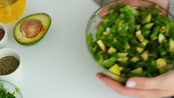 Mujer manos dando Ensalada de verduras y hierbas verdes frescas. Cocinar una dieta saludable o comida vegetariana. Menú vegano. Espinacas frescas y pepino, aguacate rúcula. Semillas de lino — Vídeos de Stock