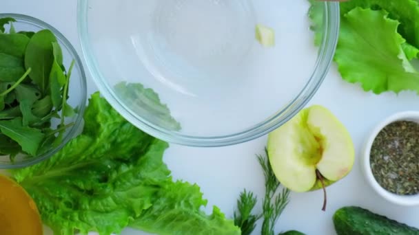 Γυναικεία σαλάτα με φρέσκα πράσινα λαχανικά και βότανα. Ακατέργαστο φαγητό. Μενού λαχανικών. Μαγειρεύοντας υγιεινή διατροφή ή χορτοφαγικά τρόφιμα. Γυναικεία χέρια κομμένα μήλο σε ξύλο κοπής που περιβάλλεται από πράσινα λαχανικά — Αρχείο Βίντεο