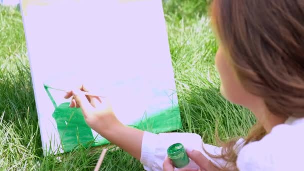 Молодая привлекательная женщина-художник рисует на природе. Палитра художников с красками и кистью Хобби. Творческий художник рисует на холсте под открытым небом. Визуальное искусство на зеленой траве в городском парке. Медленное движение — стоковое видео