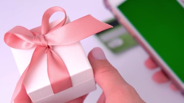 स्मार्टफ़ोन पर ऑनलाइन बैंकिंग एप्लिकेशन का उपयोग करके उपहार उपहार उपहार बॉक्स पकड़ने वाली महिला हाथ का दृश्य बंद करें और घर पर डेबिट क्रेडिट कार्ड पकड़ें। ऑनलाइन शॉपिंग छुट्टियों के लिए उपहार — स्टॉक वीडियो