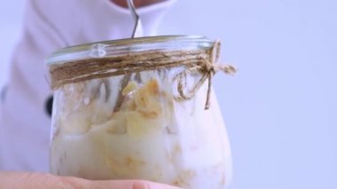 Kadın eli, sağlıklı kahvaltı yapan bir kadın. Yavaş çekimde yulaf ezmesi, Yunan yoğurdu ve fındıklı müsli ile kavanozda. Vejetaryen, vejetaryen ve kilo verme diyeti. Detox menüsü.