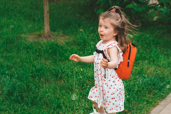 Een vrolijk meisje vangt zeepbellen met haar handen en lacht. Gelukkige jeugd, zomertijd. Portret van een jong peutermeisje — Stockfoto