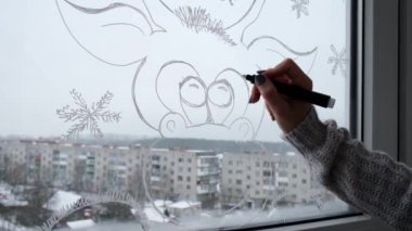 Kadın eli pencere camına Noel tatili süsü çizer. Geyik Yeni Yıl manzarasının yanında kar taneleri. hygge, dekorasyon ve noel konsepti