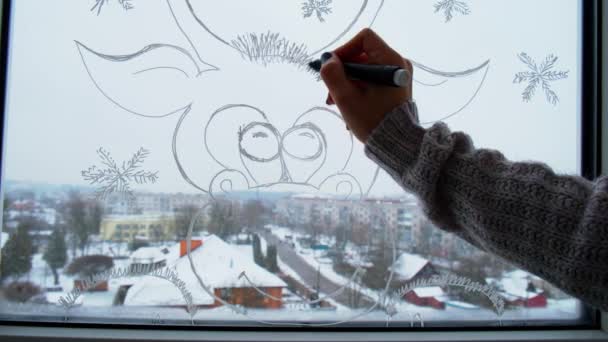 La mano femenina dibuja la decoración de las fiestas de Navidad en el cristal de la ventana. copos de nieve junto al paisaje de Año Nuevo de los ciervos. hygge, decoración y concepto de Navidad — Vídeo de stock