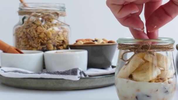 Desayunos saludables en cámara lenta. Hembra mano preparando la cocción de avena Granola con yogur griego y nueces de plátano muesli en frascos sobre fondo claro. Vegano, vegetariano y pérdida de peso concepto de dieta. Desintoxicación — Vídeos de Stock