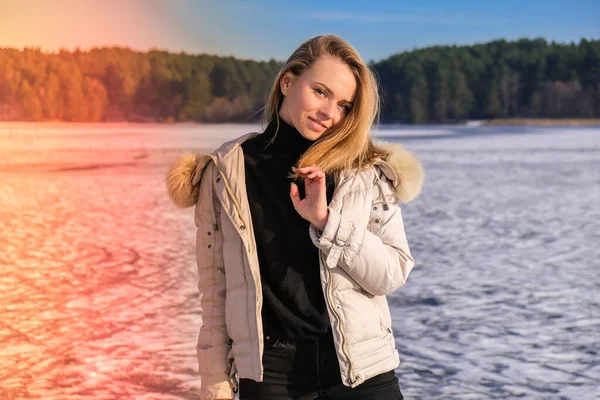 Jeune femme souriante et regardant une caméra dans un paysage enneigé. Joyeux hipster girl avec des vêtements d'hiver chauds hip hop. Rester sur la rivière gelée, lac. — Photo