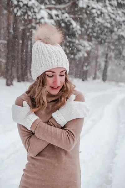 Noel, tatil ve sezon konsepti. Genç mutlu kadın kış ormanlarında kar üflüyor. Sıcak giysi, eldiven ve şapka.. — Stok fotoğraf