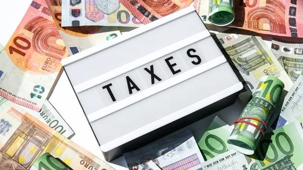 在欧元钞票周围用黑色字母写着 Taxes 字样的光盒板 纳税和申报概念 储蓄和腐败 现金结单 — 图库照片