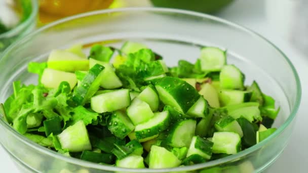 妇女烹调新鲜绿色蔬菜和香草沙拉。生的食物概念。一个菜单。烹调健康饮食或素食。雌性手在被绿色包围的木板上切黄瓜 — 图库视频影像