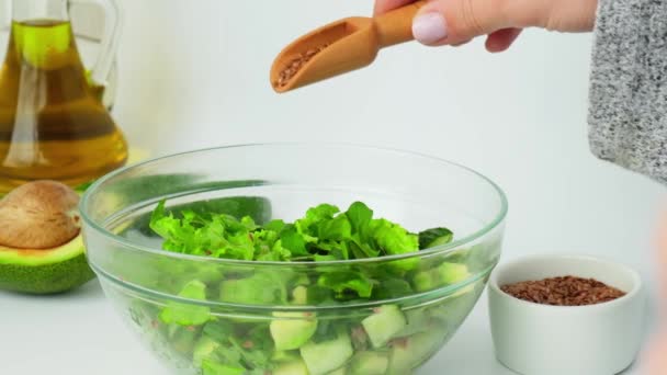 Mujer cocinando ensalada de verduras y hierbas verdes frescas. Cocinar una dieta saludable o comida vegetariana. Las manos femeninas añaden semillas de lino. Receta paso a paso. — Vídeo de stock