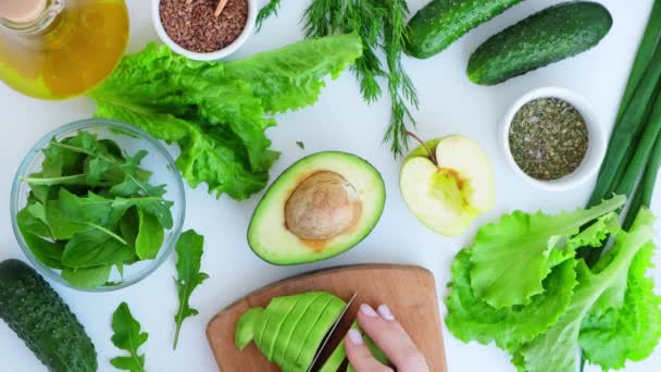 Femme cuisine salade de légumes verts frais et d'herbes. Concept de nourriture crue. Menu végétalien. Cuisiner une alimentation saine ou végétarienne. Mains féminines coupées avocat sur planche à découper entourées de légumes verts — Video