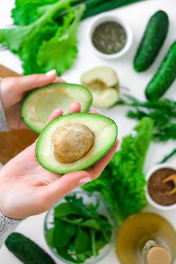 Taze yeşil sebze ve ottan salata pişiren bir kadın. Sağlıklı beslenme ya da vejetaryen yemekleri pişirmek. Kadın elleri yeşil sebzelerle çevrili avokadoyu tutar. Adım adım tarif et. Sağlıklı beslenme. Salata için malzemeler. Sağlıklı sebzeli düz desen.