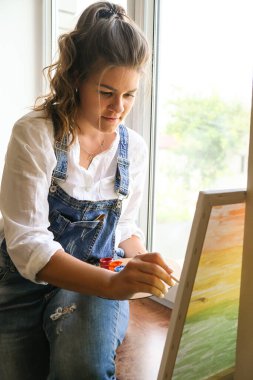 Çalışan yaratıcı bir ressam. Sanatçı işyeri, hobi, el sanatları aletleri. Sanatçı kadın tuval resmi. Atölyede profesyonel genç kadın ressam çiziyor. Boş zaman aktivitesi. Evde sanat